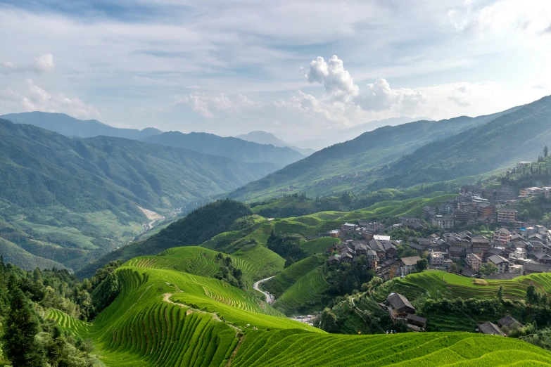 a scenic valley with several buildings on the edge and mountains in the background