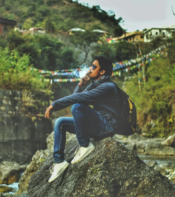 a young man sitting on a rock drinking soing