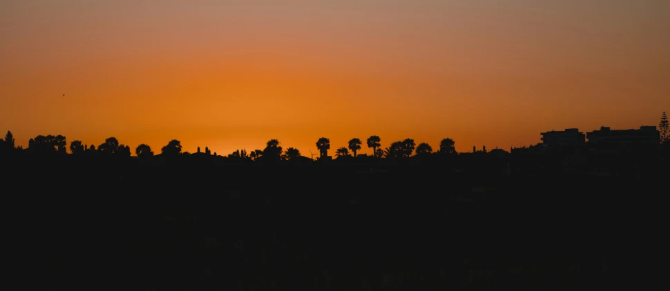 the sun is setting in the background with silhouettes of buildings