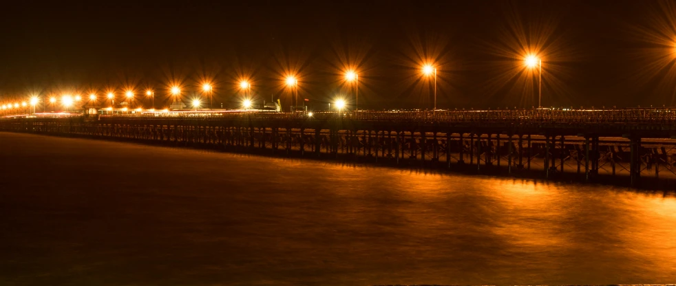 a night scene of a pier with lights on and water in the foreground