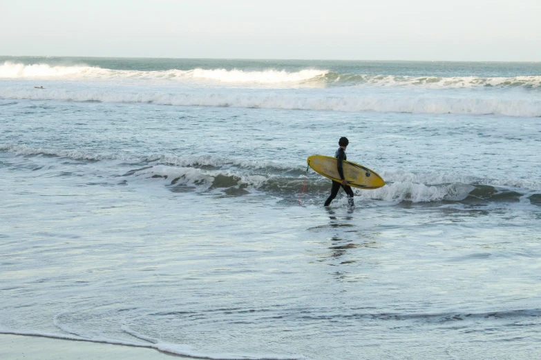 the man is walking in the surf carrying his surfboard