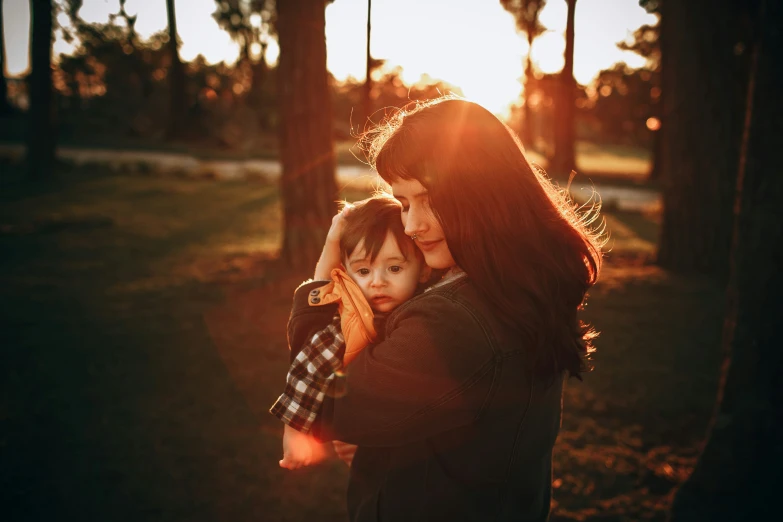 a woman holding her child in a park at sunset