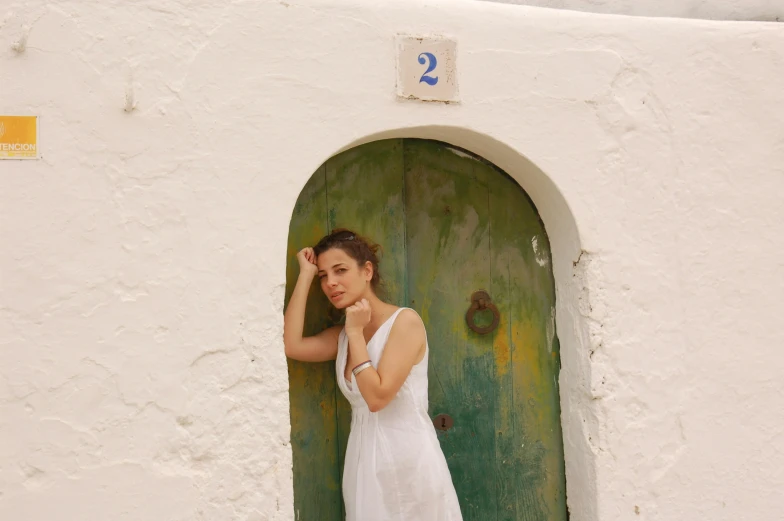 a woman poses in a doorway outside of a whitewashed building