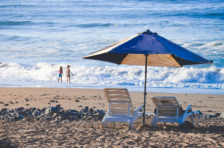 two chairs and umbrella on the beach by the water