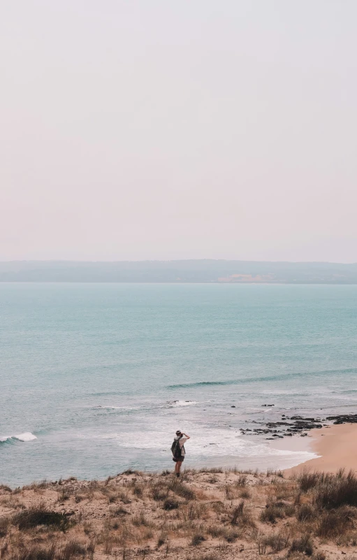 a man standing at the edge of a beach near the ocean