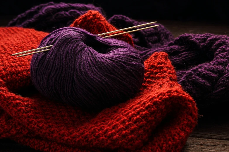 a purple yarn is next to some red wool