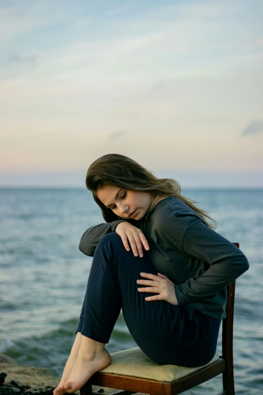 a girl sitting on a chair in front of the ocean