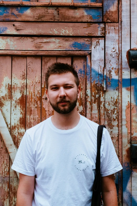 a bearded man stands in front of a wall of paint