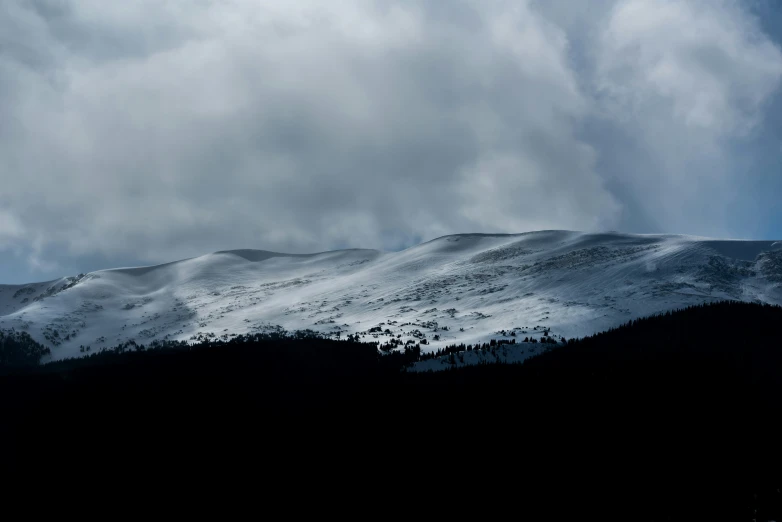 a snowy mountain with dark clouds in the sky