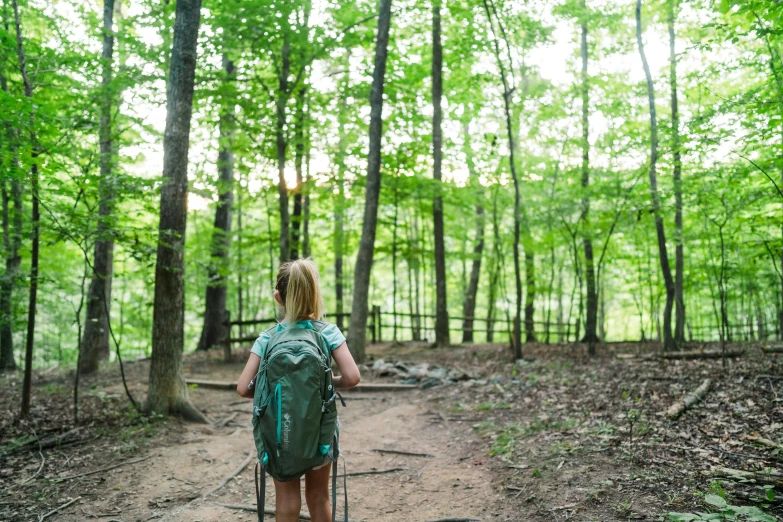 a woman with green backpack and skis stands in a forest path