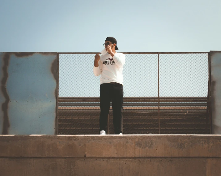 a person standing by a fence talking on the phone