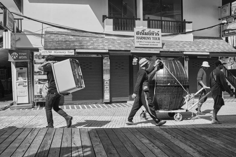 three men carry carts down a sidewalk in the city