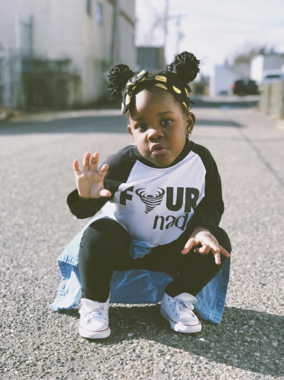 a small child sitting on the ground wearing jeans and a tee shirt