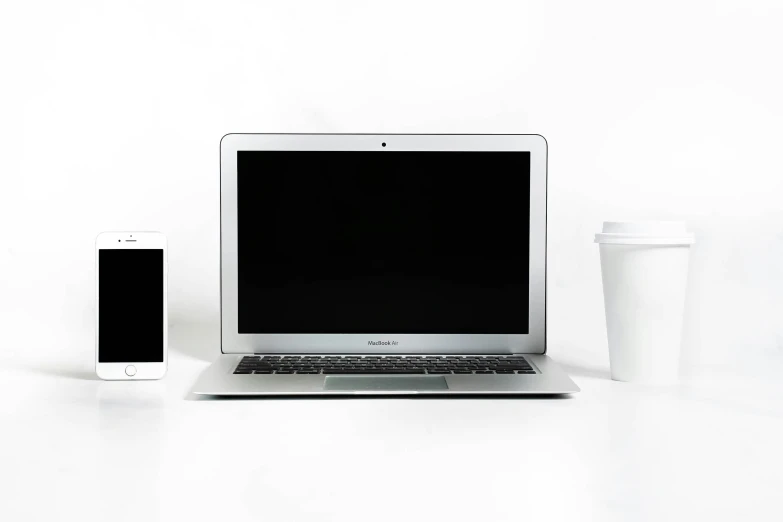 a laptop, cup, and cell phone sitting on a desk