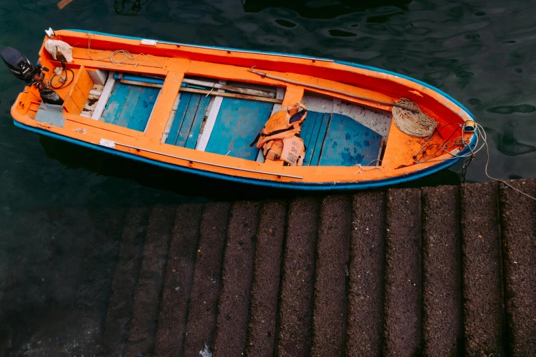 an orange and blue boat floating in water next to dock