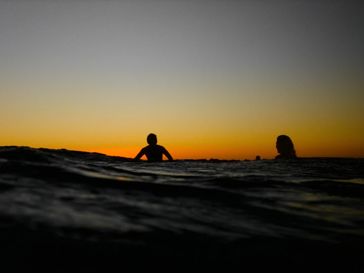 two people are swimming in the ocean at sunset