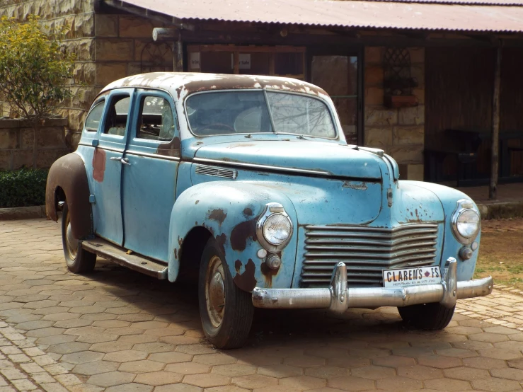 an old rusty blue car parked in front of a brick building