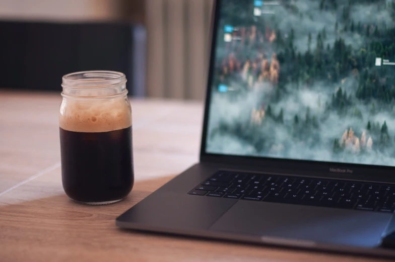 a glass jar with dark liquid next to a laptop computer