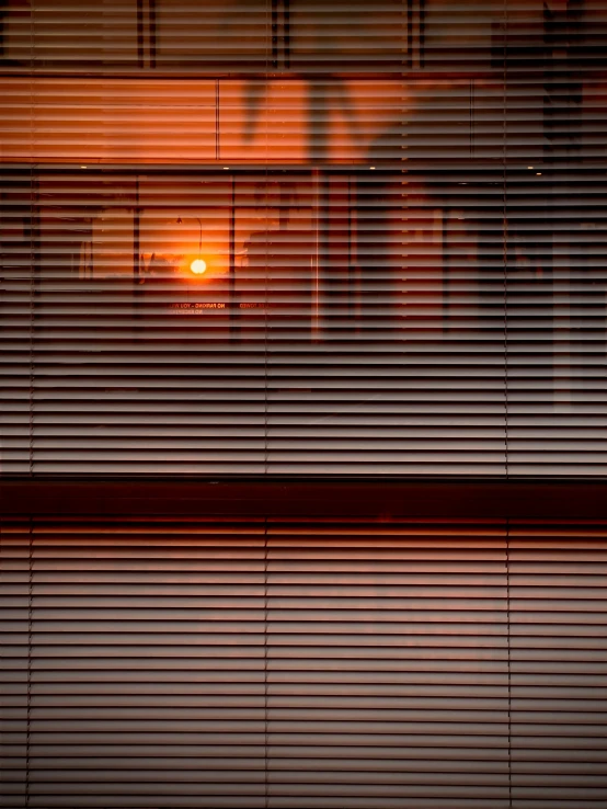 the sun is setting behind a window with blinds