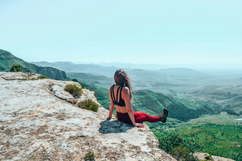 the woman is sitting on a cliff looking at the mountains