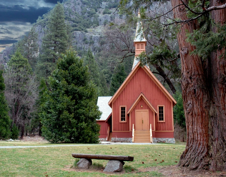 a small red church with steeple near a tree