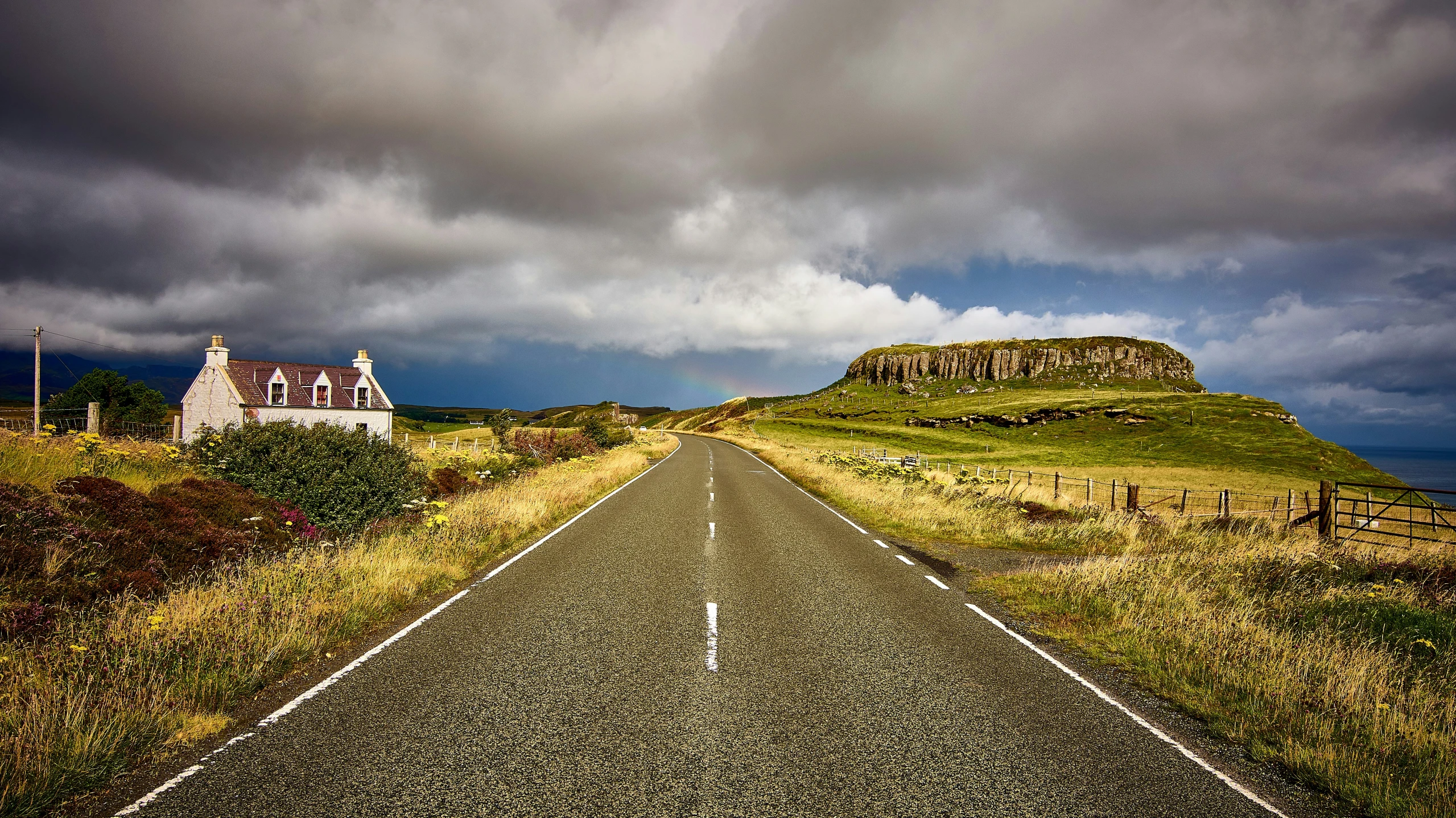 a deserted road on a hill that is surrounded by fields and a small white house