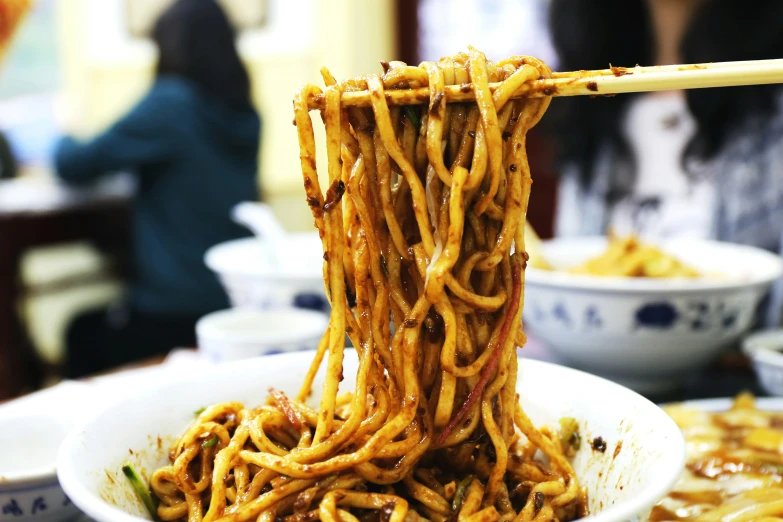 chopsticks are being held over a bowl of food with noodles