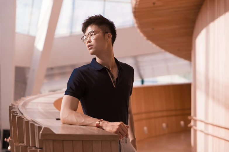 a young asian man wearing glasses and a black shirt standing in an empty auditorium