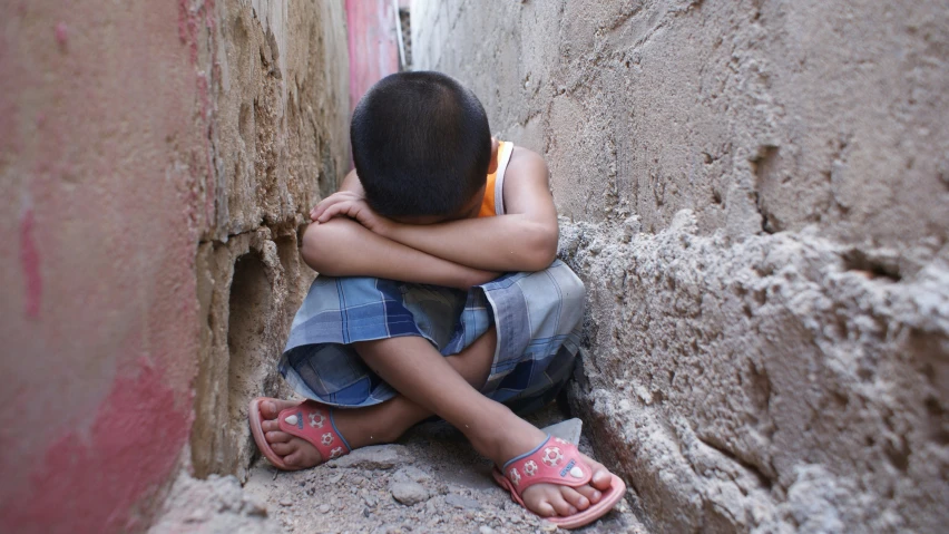 a  sitting against a stone wall wearing sandals