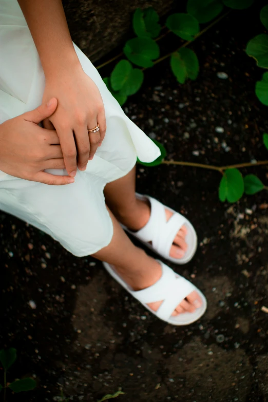 a woman in white sandals holding her hand on top of her leg