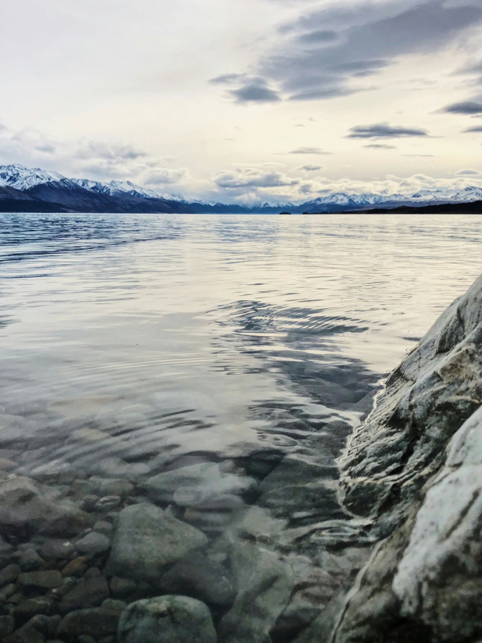 a rocky shore with calm water and the mountains in the background