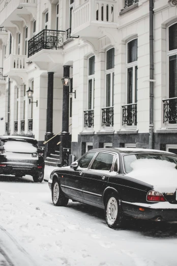 cars driving in snow on the road, near a building