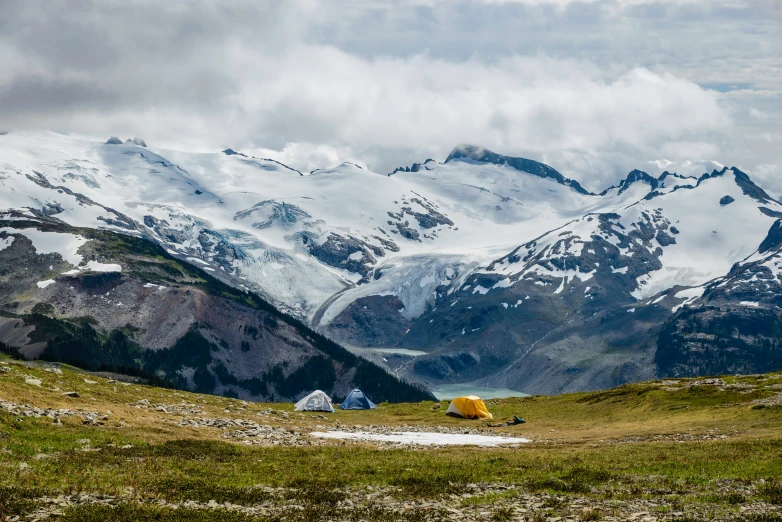 some snow mountains and a field with yellow tents