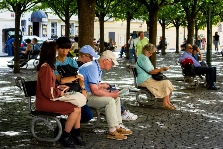 the older man in blue shirt is on his laptop while sitting on the park bench