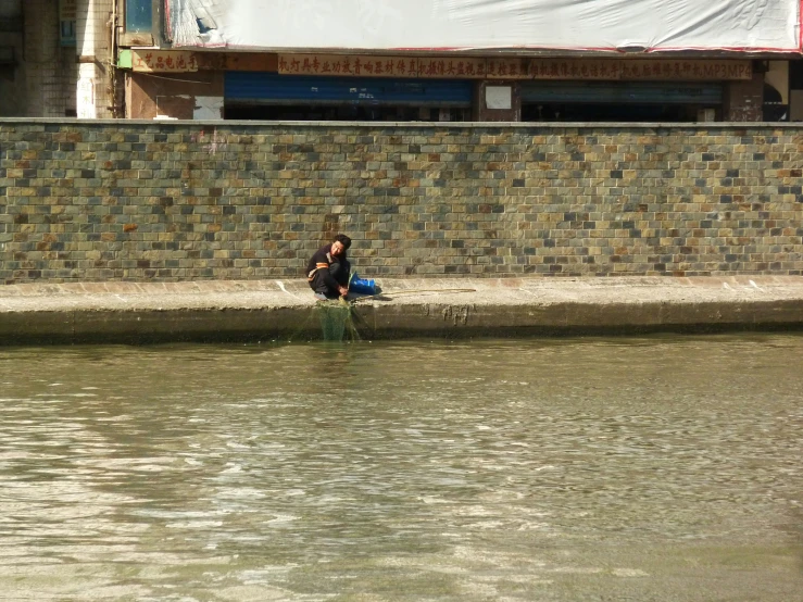 a person sitting on the edge of a wall next to a river