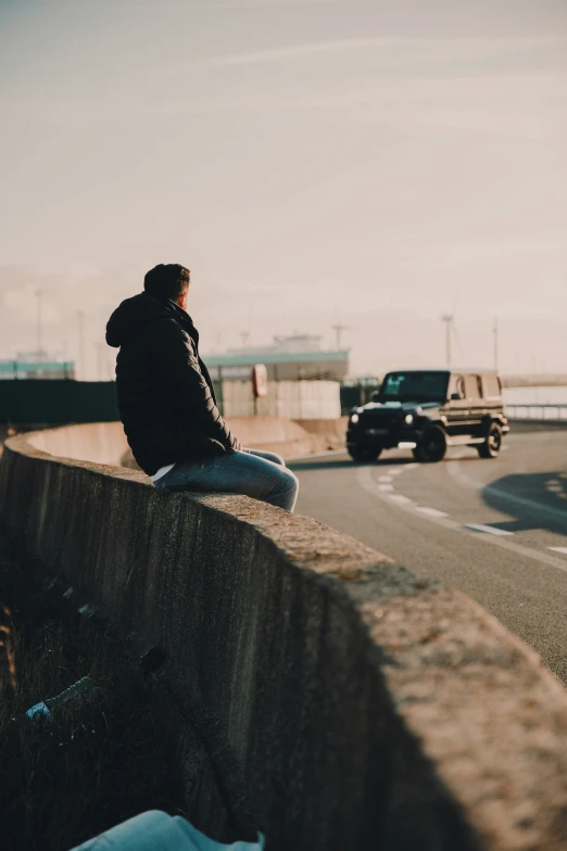 a person on the side of a road sitting and looking at a vehicle driving in the background