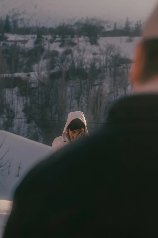 a person with a hood on looking at another man in the snow