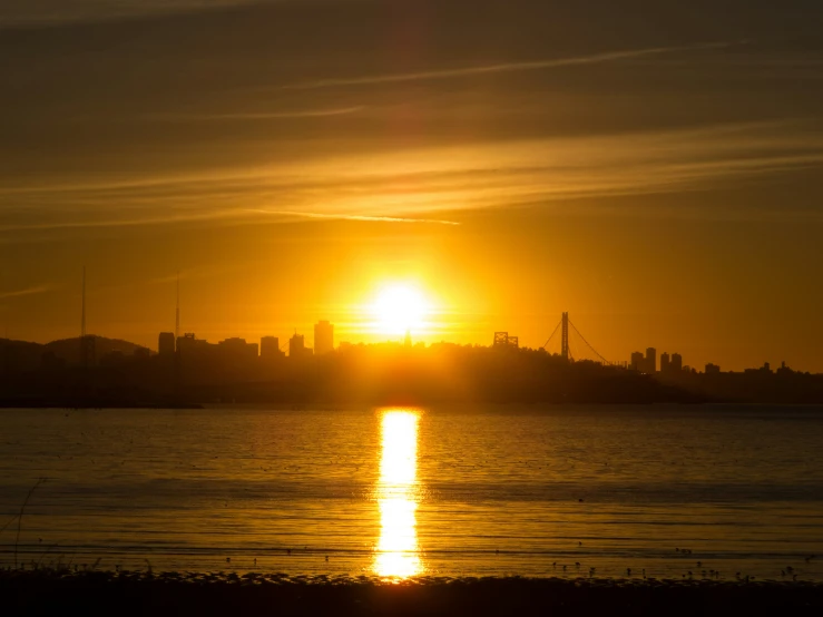 the sun rises over an urban skyline on the other side of a bay