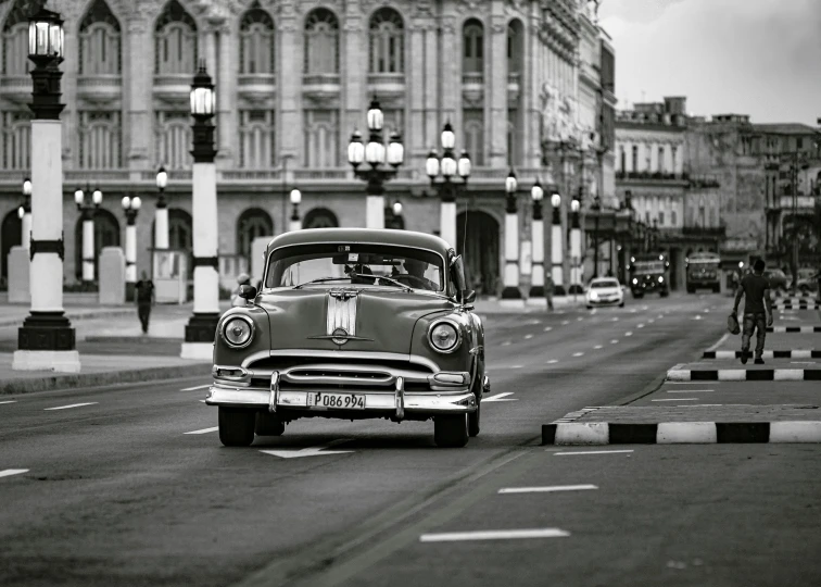 a black and white image of an old car driving on the road