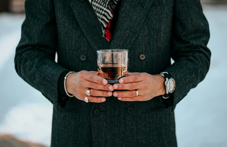 a man wearing rings and a tie holding a glass of wine