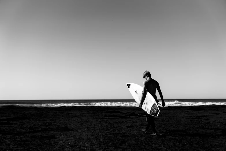 a man in a wetsuit walking along the beach with his surfboard