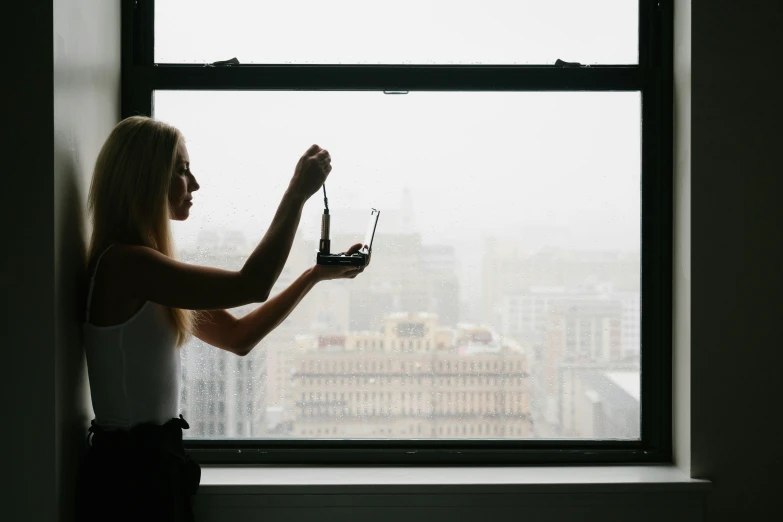 a woman standing next to a window holding a remote