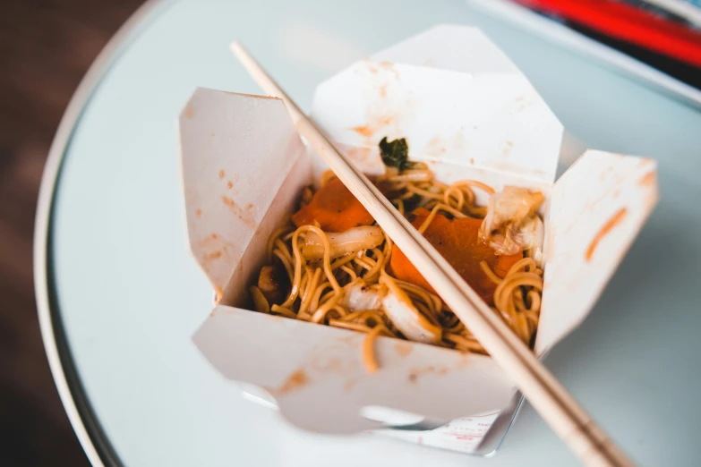 a square box with noodles and chopsticks on the table