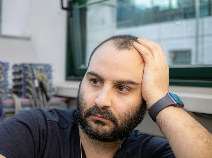 man with hands on head sitting against window