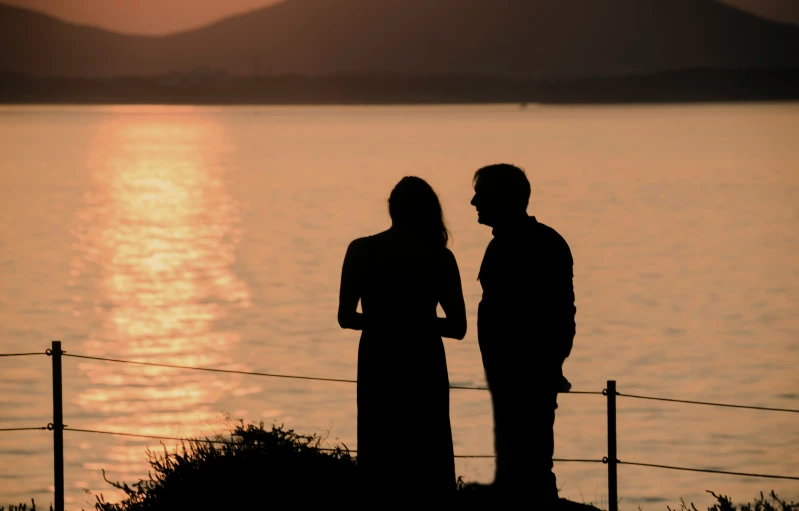 a silhouette of a man and a woman standing by the water