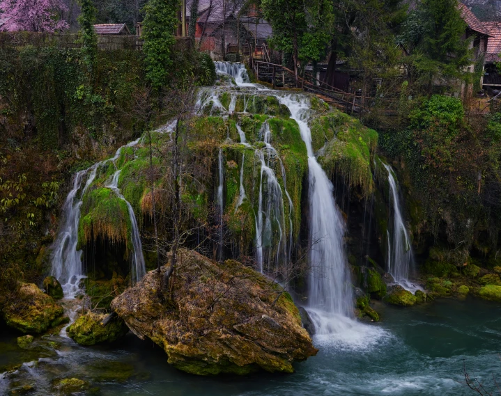 a waterfall flowing over moss covered rocks near trees