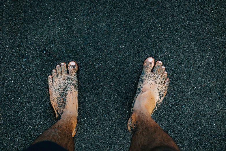 bare feet standing on sandy beach area next to dark colored water