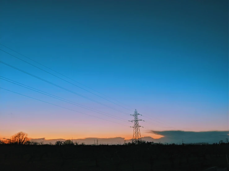 telephone wires are silhouetted against a dark blue sunset