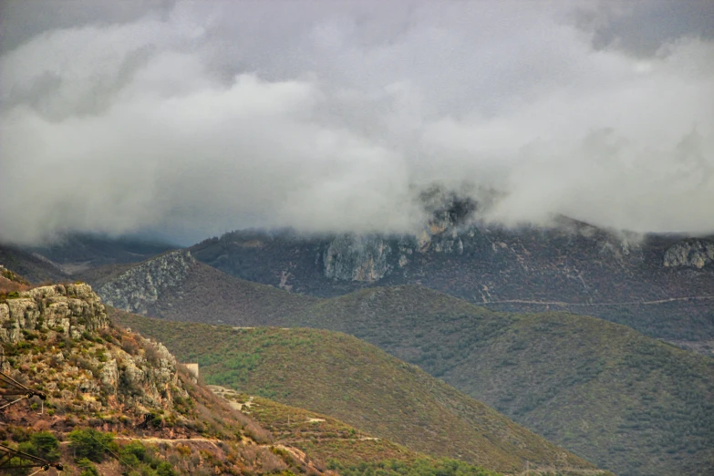 a mountain side road near some mountains under a cloudy sky