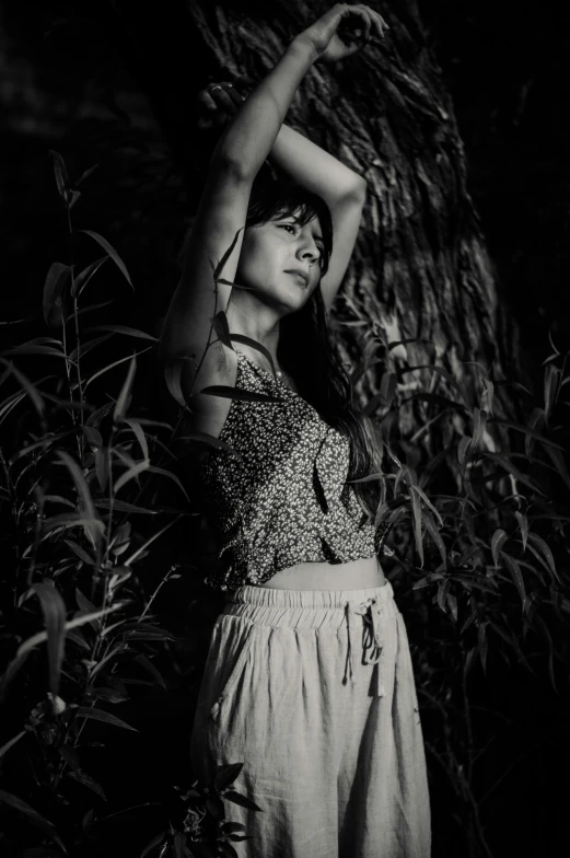 black and white pograph of woman with arms extended standing next to a tree